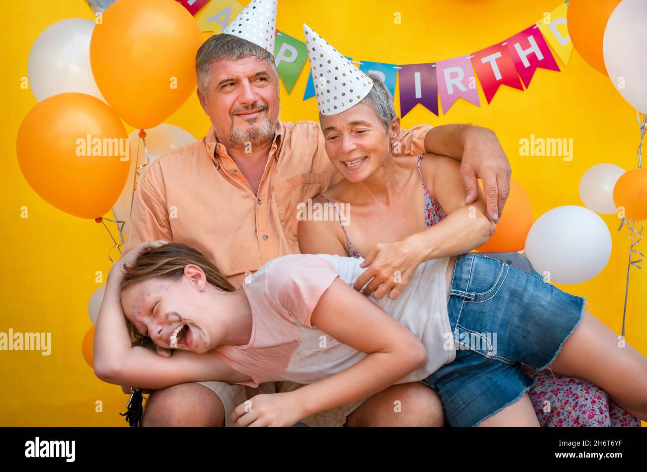 Familienportrait auf gelbem Hintergrund. Das Mädchen legte sich auf die Knie ihrer Eltern Stockfoto