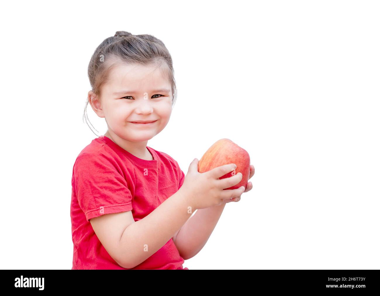 Kind mit rotem Apfel isoliert auf weißem Hintergrund. Mädchen schaut auf die Früchte und lächelt Stockfoto