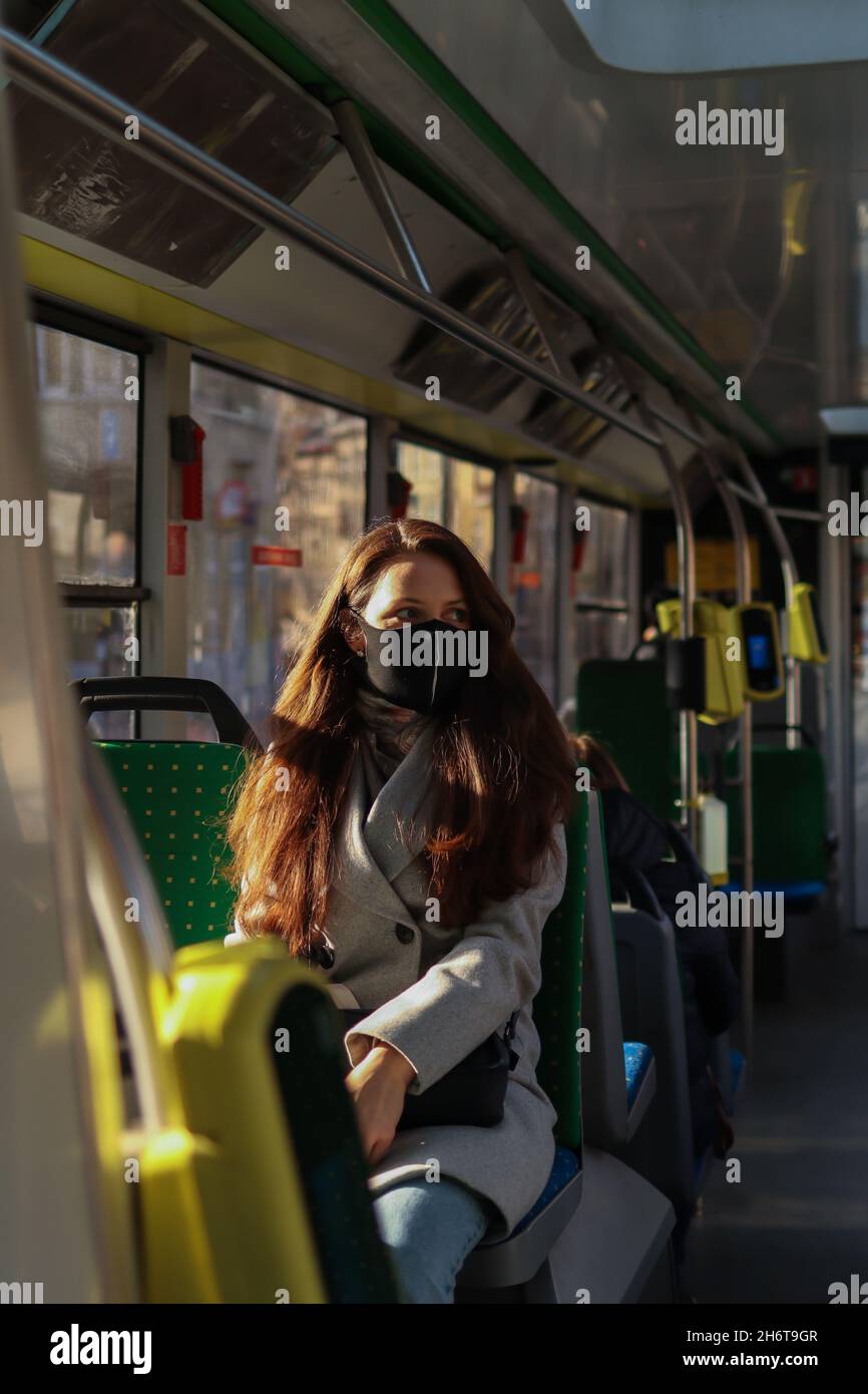 Junge europäische Passagierin mit Gesichtsmaske, wenn sie während der Pandemie von Covid-19 mit dem Bus an überfüllten Orten unterwegs ist. Stockfoto