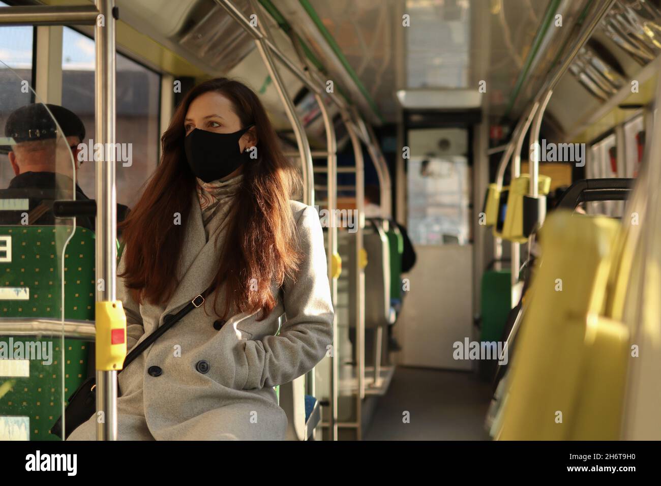 Mehrjährige kaukasische Menschen in Gesichtsmasken-Schutz fahren in einem Bus. Junge tausendjährige Frau, die im öffentlichen Nahverkehr auf das Fenster schaut. Stockfoto