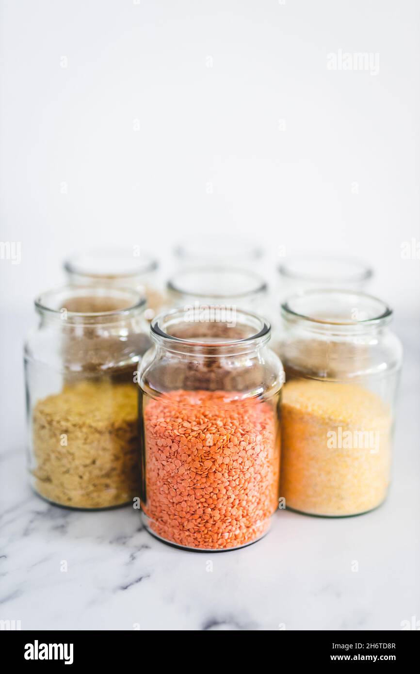 Gesunde Vollkornprodukte und Hülsenfrüchte in durchsichtigen Pantry-Gläsern auf Marmorboden, inklusive Quinoa-Reis-Buchweizen-Linsen und Gerste, einfache vegane Pantry Stockfoto