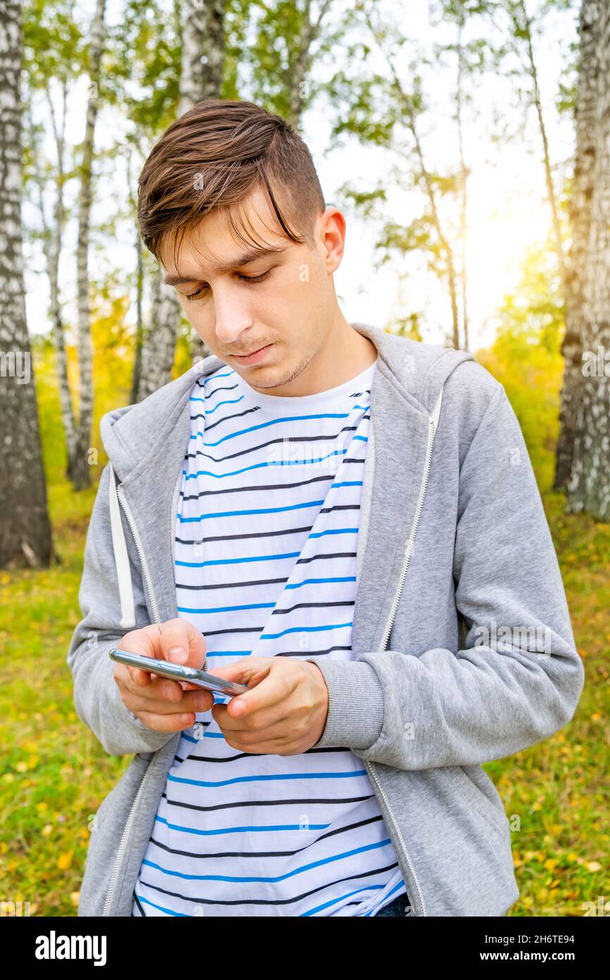 Junger Mann hält ein Mobiltelefon im Herbstwald Stockfoto