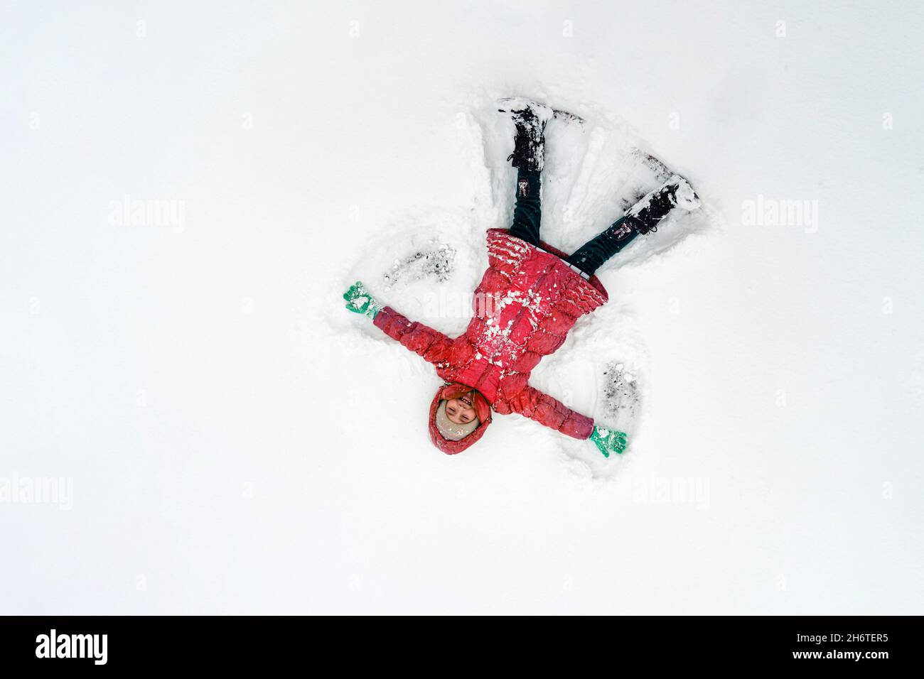 Aktive Kinder in einer roten Jacke im Freien am Weihnachtstag. Kind macht Schnee Engel am sonnigen Wintermorgen. Kinder im Winter Spaß im Freien. Familienweihnachtsurlauber Stockfoto