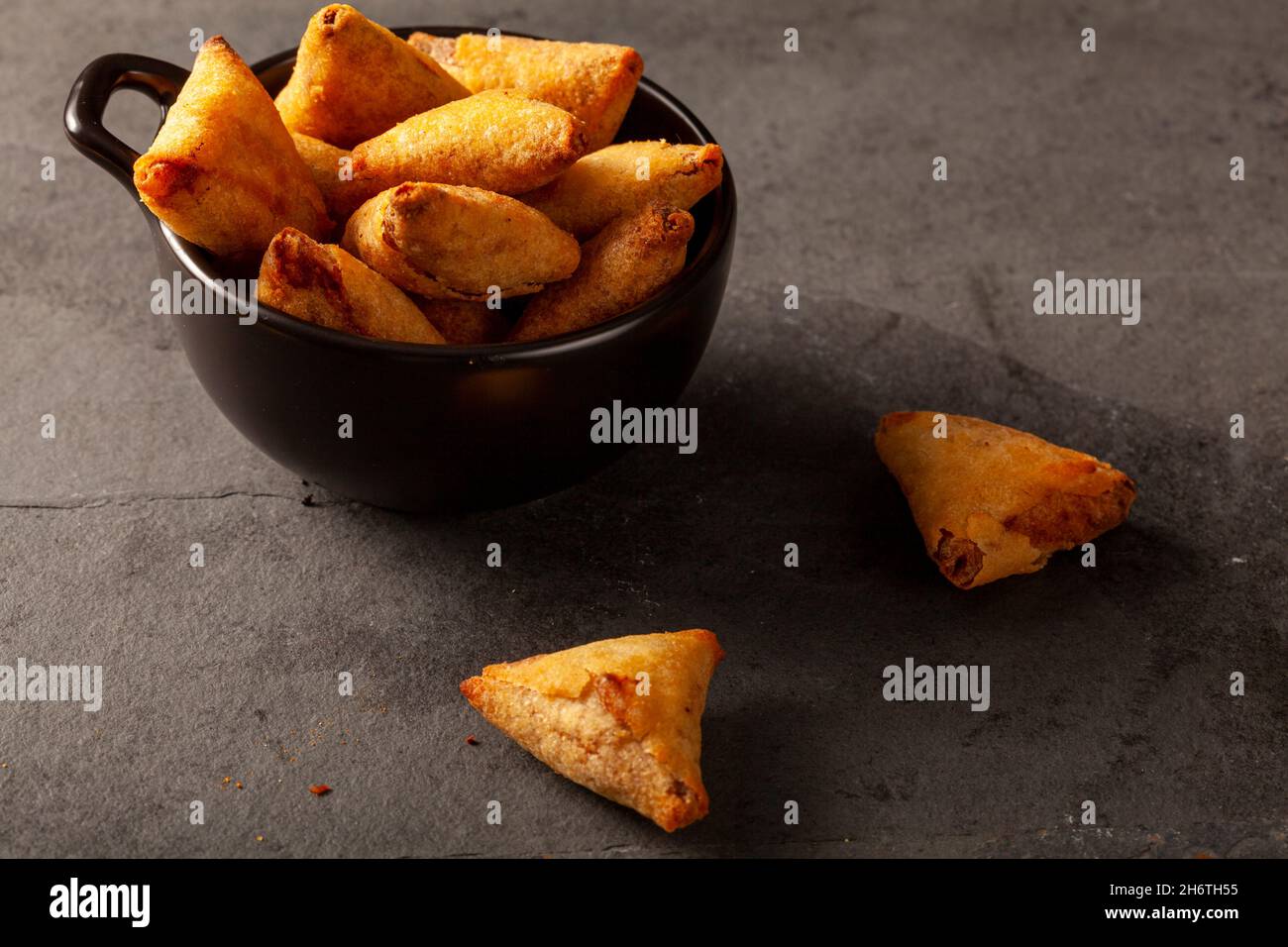 Dunkles Hintergrundbild mit schwachem Licht, das eine Nahaufnahme der traditionellen indischen Samosa zeigt, einer frittierten dreieckigen Pastete, gefüllt mit herzhaften Zutaten wie z. B. c Stockfoto