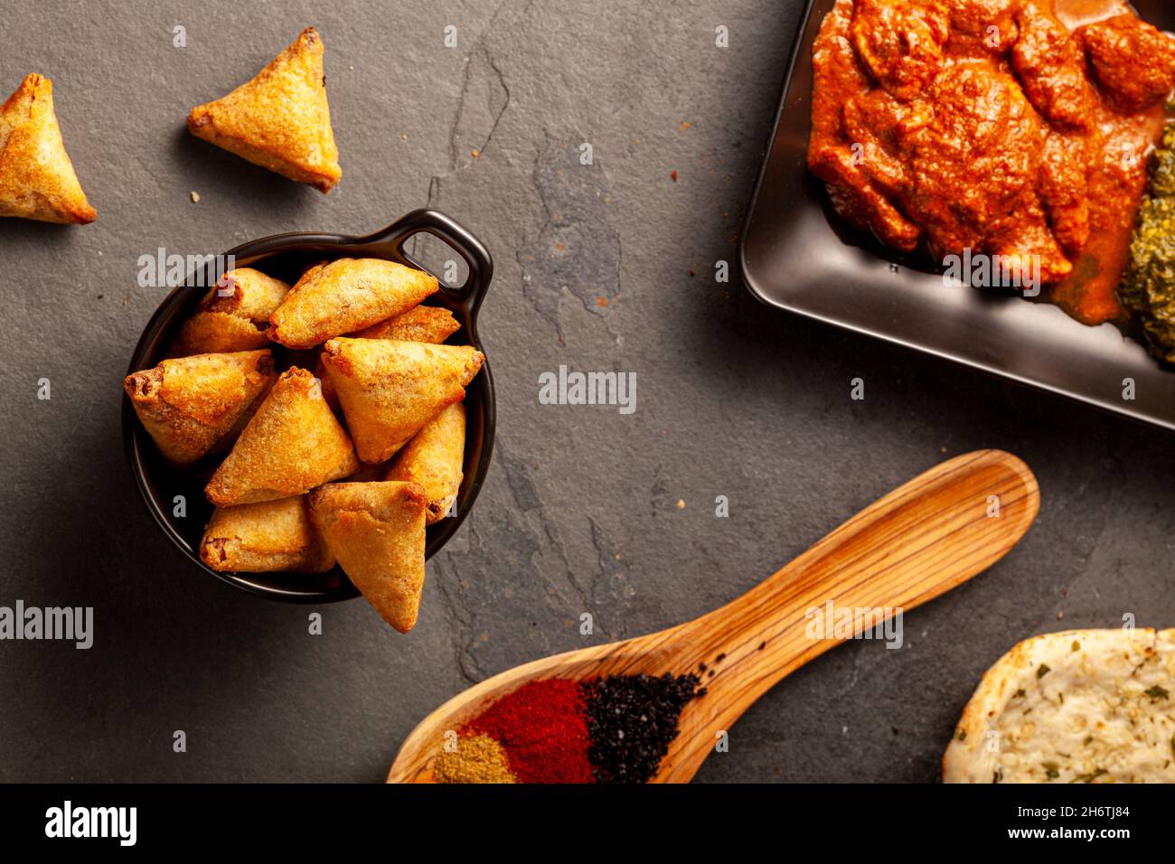 Nahaufnahme eines Tisches mit köstlichen Gerichten aus Indien. Dunkler Hintergrund mit Naan, Hühnchen, Palak Paneer, Samosa, verschiedenen Gewürzen a Stockfoto