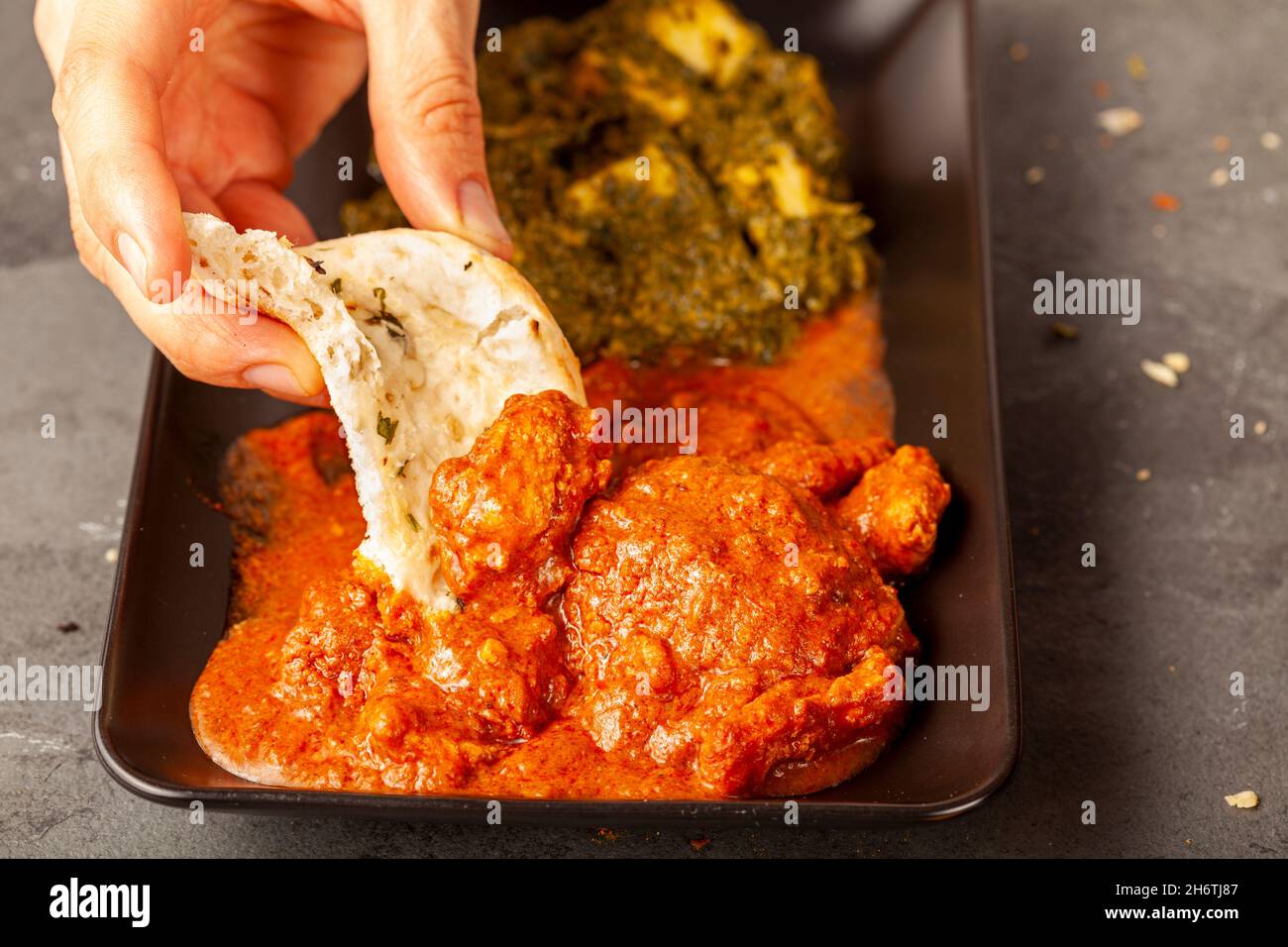 Eine Frau isst leckeres indisches Essen mit verschiedenen Gerichten. Sie taucht Naan-Brot in ein frisches Brot. Konzept für die Vielfalt der asiatischen Küche. Tikka Masala und Stockfoto