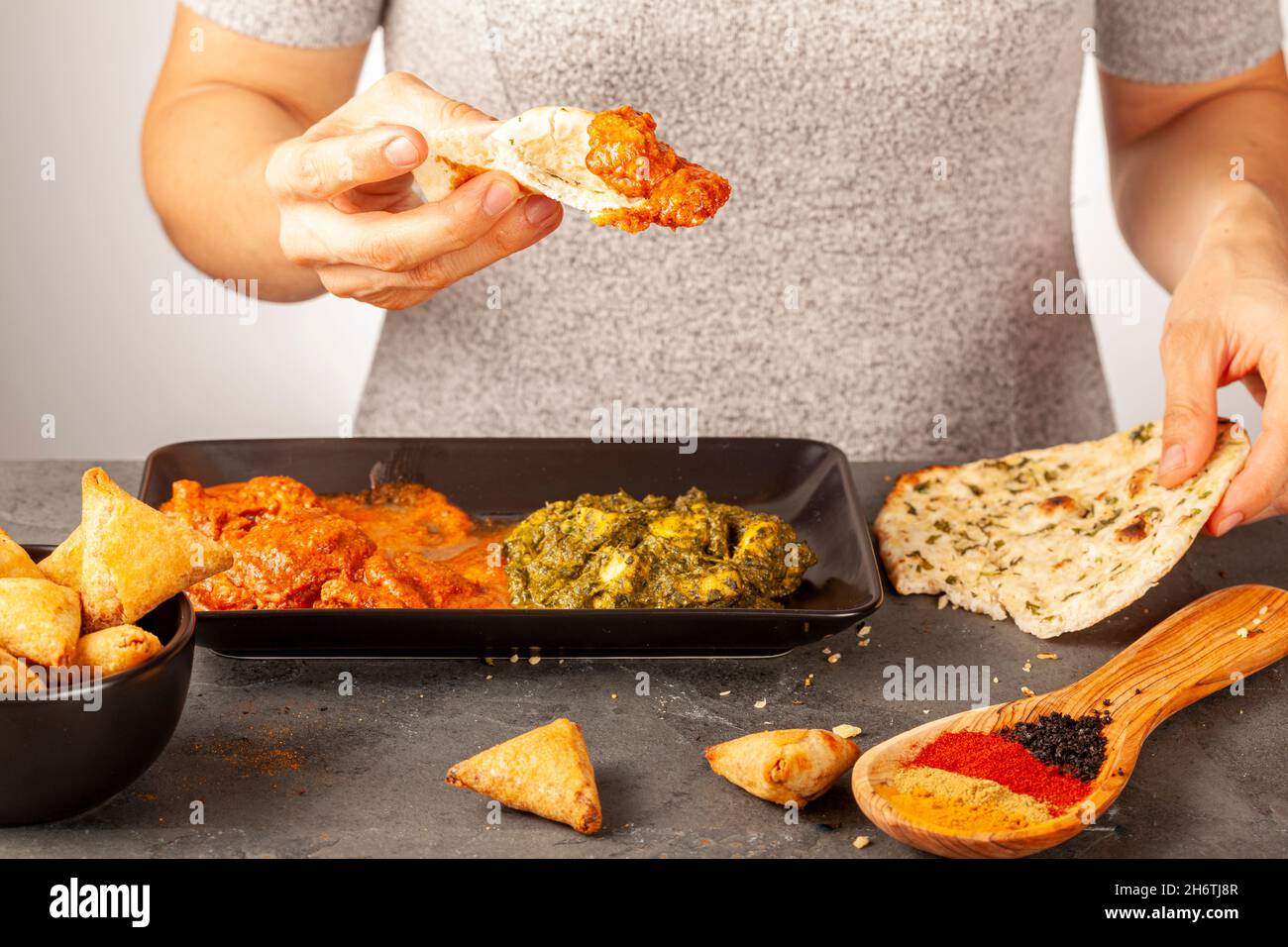 Eine Frau isst leckeres indisches Essen mit verschiedenen Gerichten. Sie taucht Naan-Brot in ein frisches Brot. Konzept für die Vielfalt der asiatischen Küche. Tikka Masala und Stockfoto
