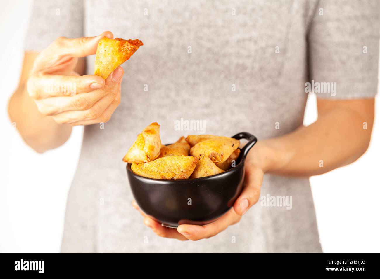 Eine Frau hält eine Porzellanschale mit indischen Samosas, dreieckigen knusprigen frittierten Snacks mit würzigen, herzhaften Füllungen. Sie isst einen. Licht und Stockfoto