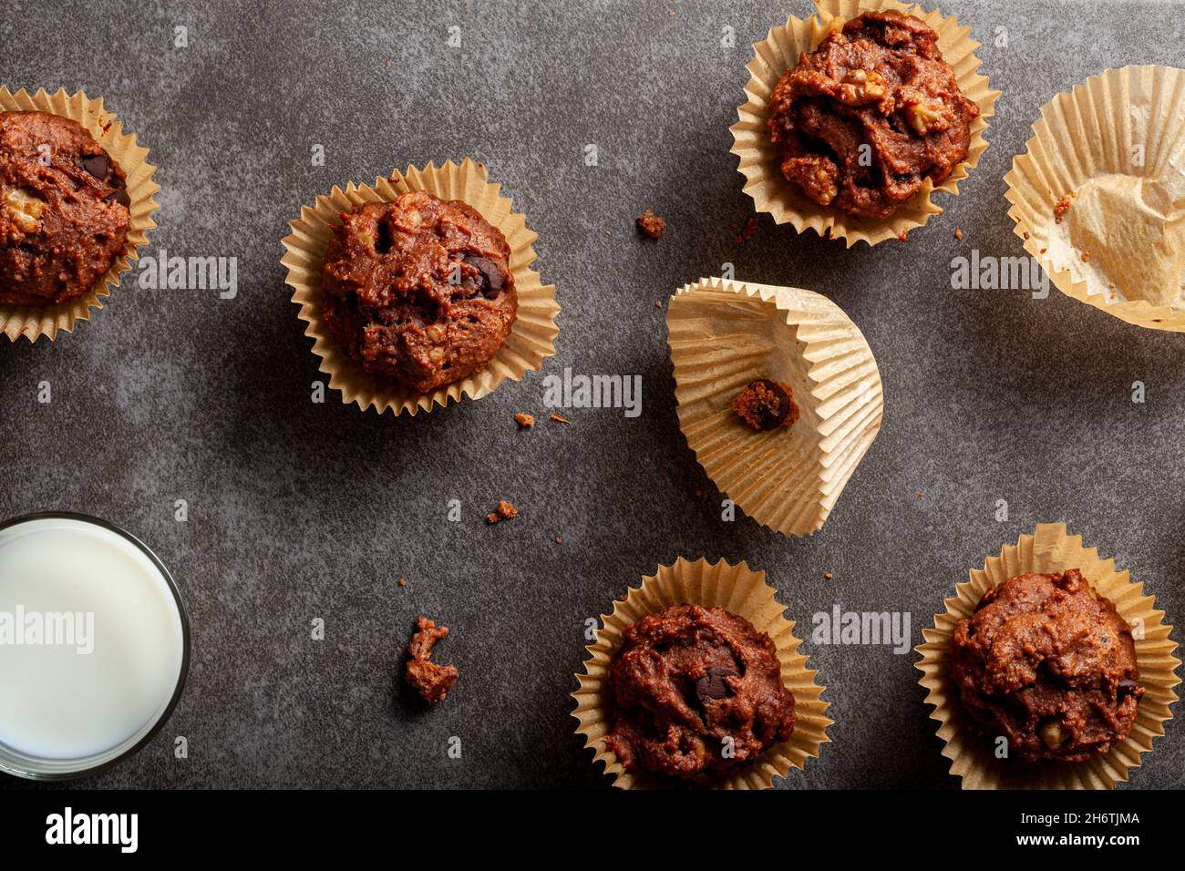 Draufsicht Bild zeigt frisch gebackene Cup Cakes in Papiereinlagen auf Stein Hintergrund. Serviert mit einem Glas Milch zum Frühstück oder Snack. Cacoa, Obst und Stockfoto