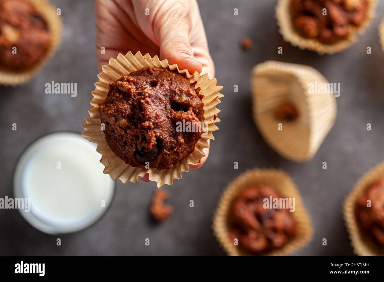 Eine kaukasische Frau hält eine frisch gebackene köstliche Schokoladennuss-Muffins auf grauem Hintergrund mit einem Glas Milch zum Dunkeln serviert. Konzept f Stockfoto
