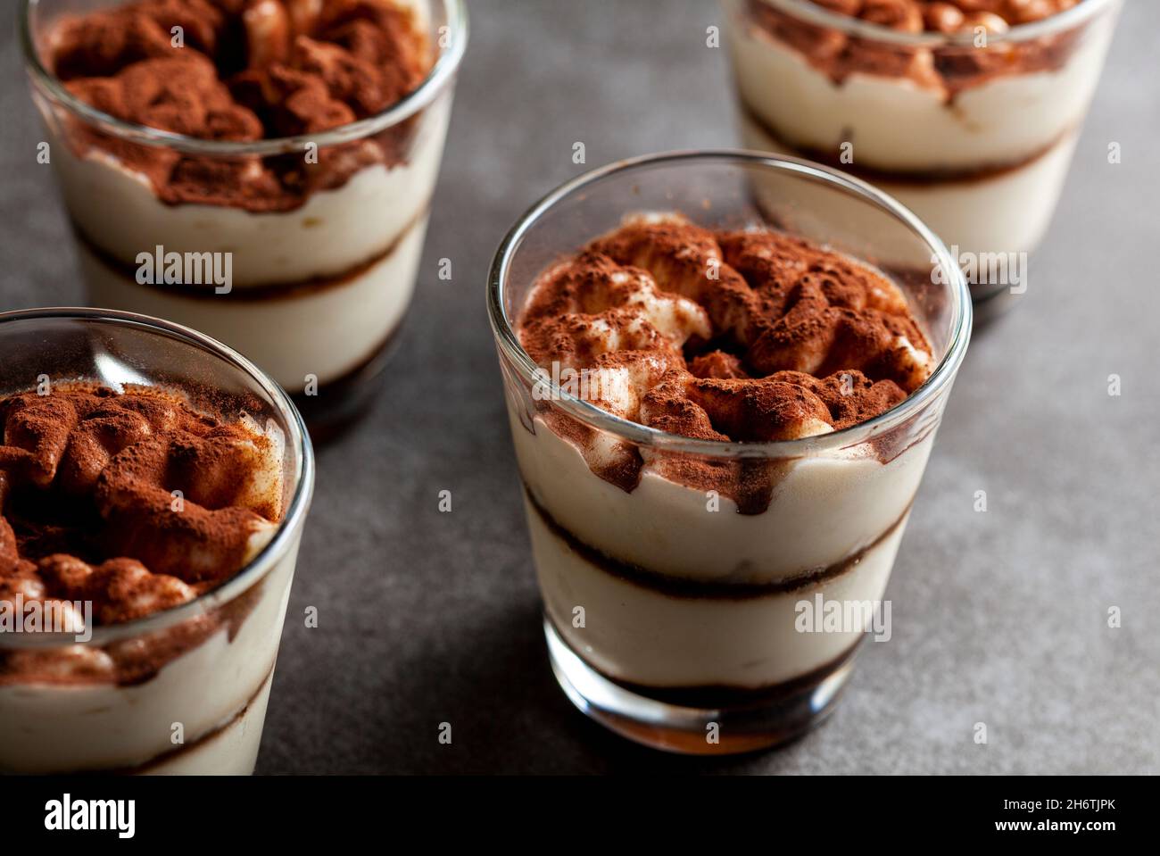Köstliche traditionelle Tiramisu-Wüste in kleinen Glasbechern auf steinerner Arbeitsplatte serviert. Das Bild bei schwachem Licht zeigt Textur und Schichten aus dem Winkel mit flacher Oberfläche Stockfoto