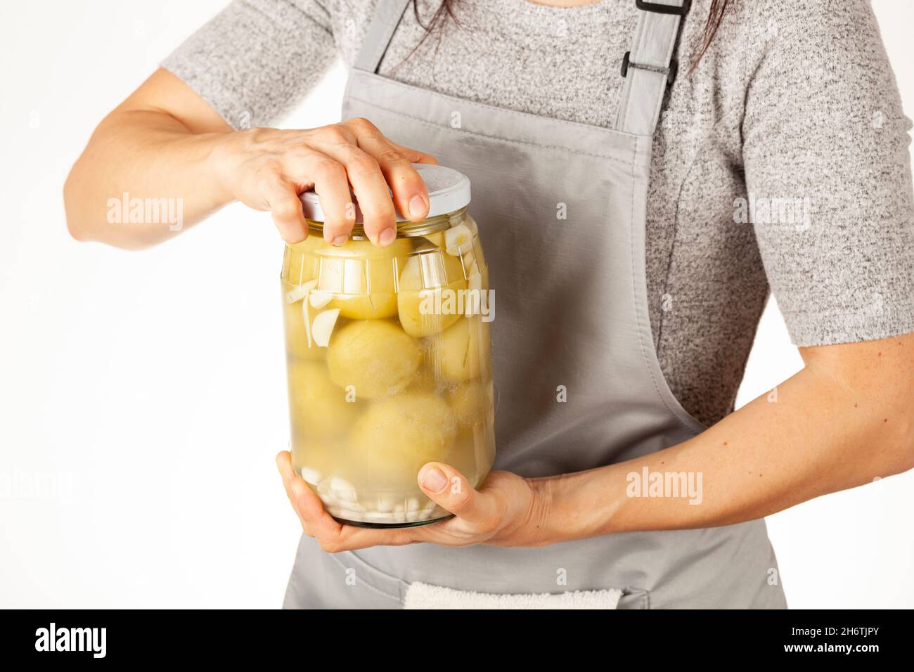 Eine kaukasische Köchin mit Schürze versucht, einen hartnäckigen Glasdeckel zu öffnen. Sie wendet Gewalt an, um den Deckel in der Küche abzuschrauben. Konzeptbild zum Beizen nach Stockfoto
