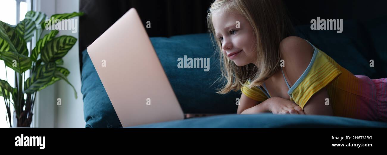 Kleines Mädchen, das auf der Couch liegt und auf den Laptop-Bildschirm schaut Stockfoto