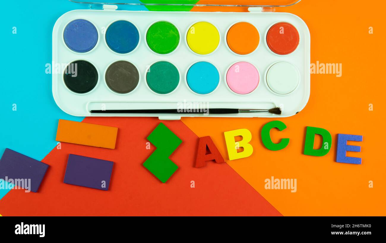 Eine Palette von Aquarellfarben, Alphabeten und Formen auf farbigem Hintergrund. Selektiver Fokus auf das Alphabet. Stockfoto