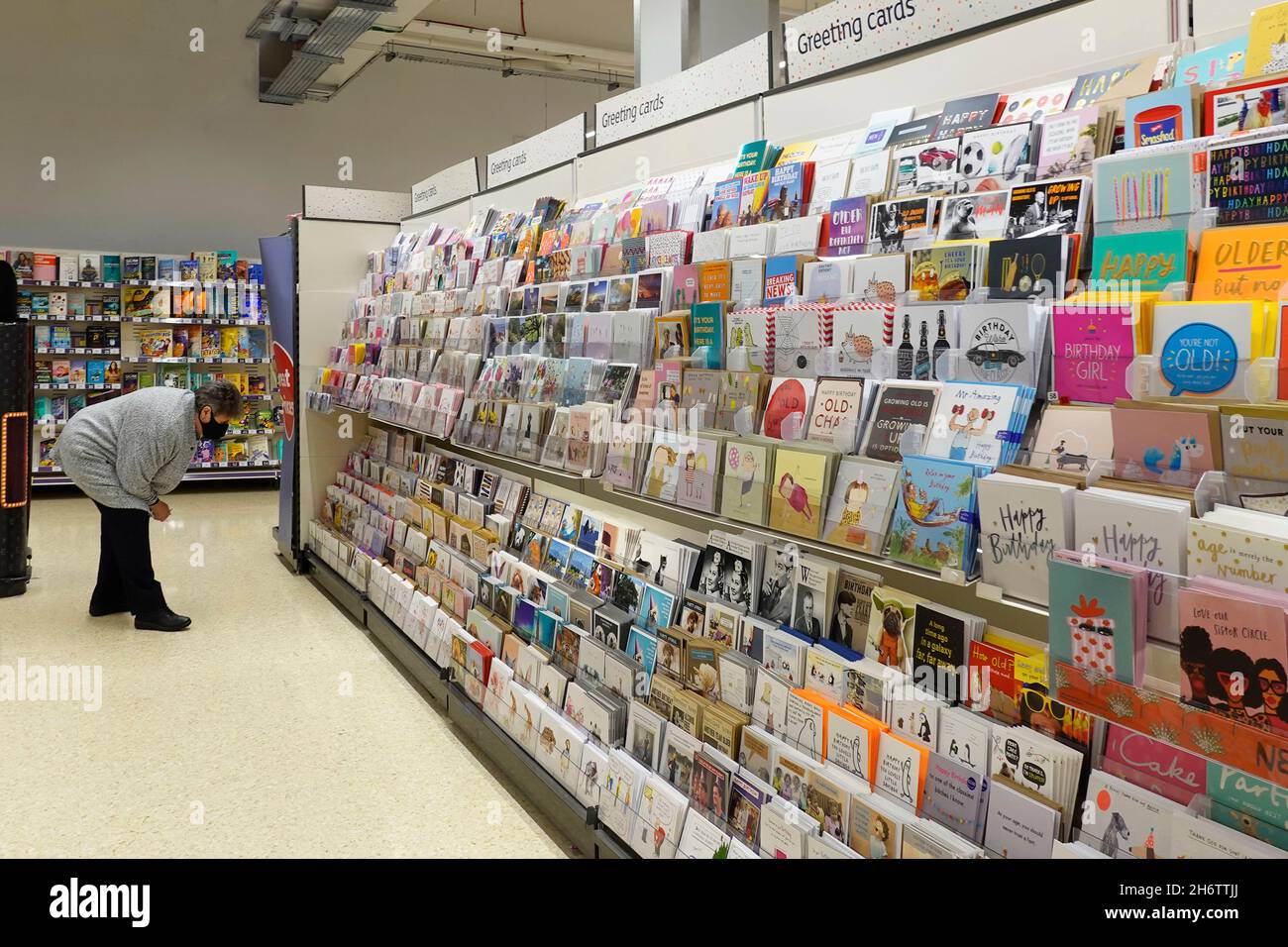 Ältere ältere Frau Shopper in Gesichtsmaske Einkaufen in einem Sainsburys Supermarkt Gang Browsen, um Nachricht auf Grußkarten-Rack auswählen England Großbritannien Stockfoto
