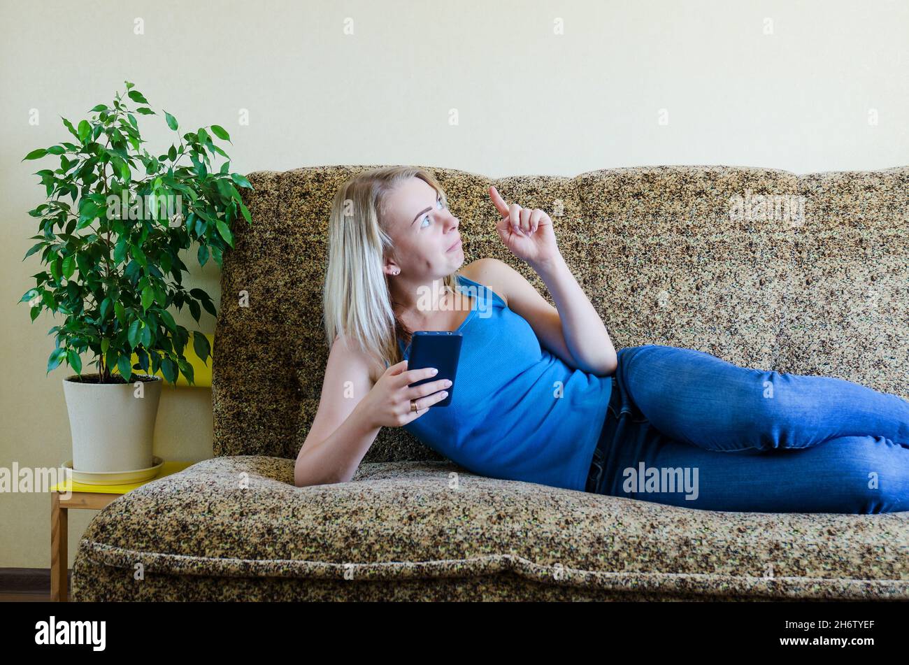Junge blonde Frau zu Hause auf der Couch sitzen, entspannen. Arbeiten auf dem Mobiltelefon von zu Hause aus. Glücklicher Familienleben, Hobby und Freizeit. Geschäftsfrau Stockfoto