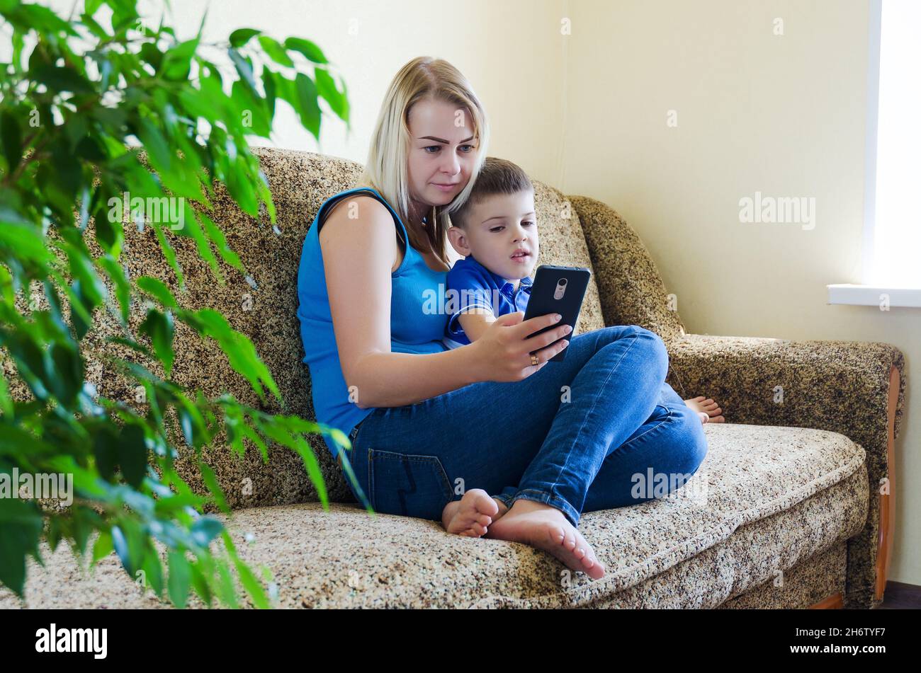 Mutter und kleines müdes Kind, Junge zu Hause auf der Couch sitzend, mit Laptop, entspannen. Arbeiten von zu Hause aus. Glücklicher Familienleben, Hobby, Freizeit. Unternehmen Stockfoto