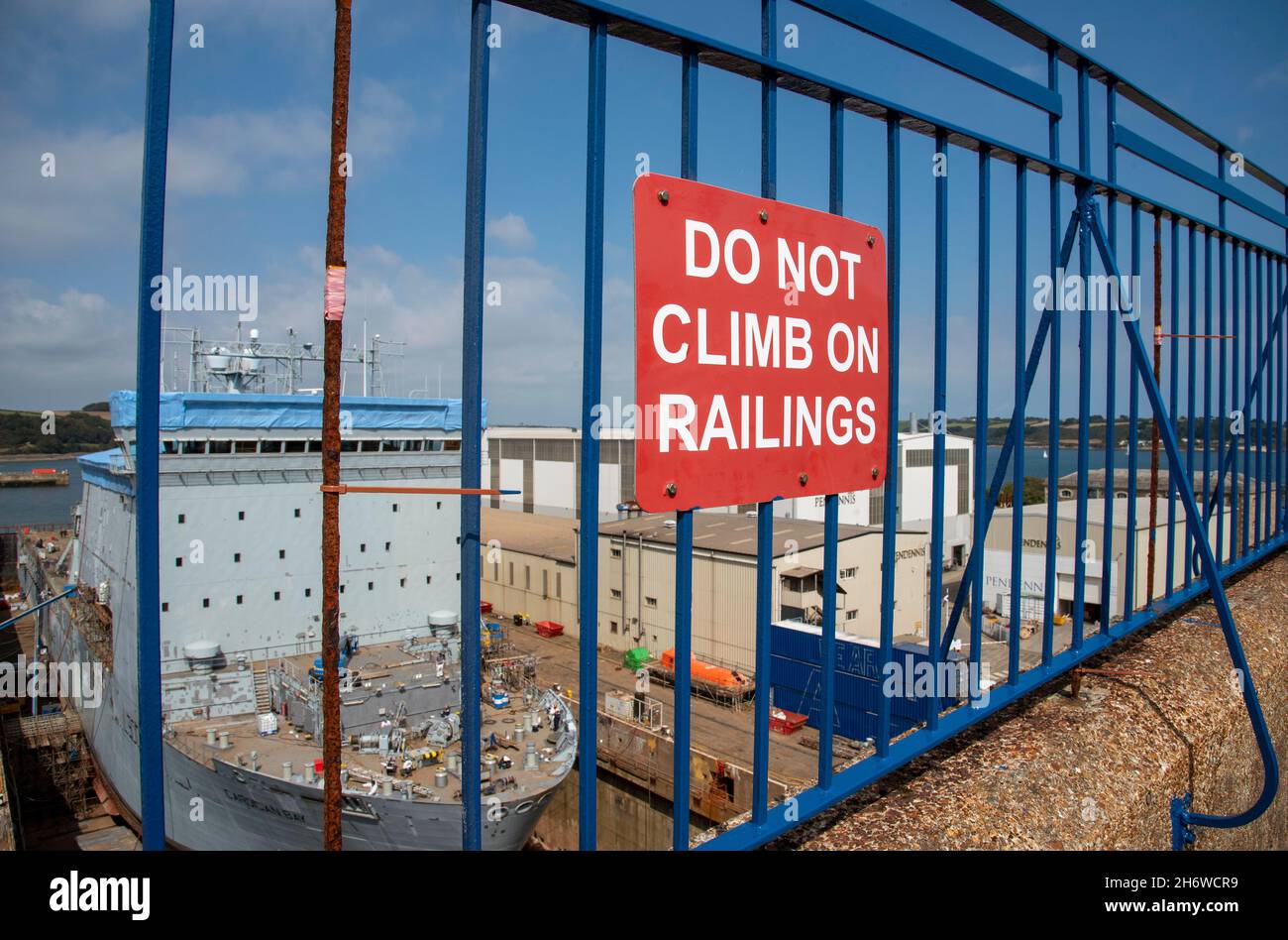 Cornwall, England, Großbritannien. 2021. Steigen Sie nicht auf Railings Zeichen auf einem blau lackierten Metallzaun mit Blick auf ein Industriegebiet. Stockfoto