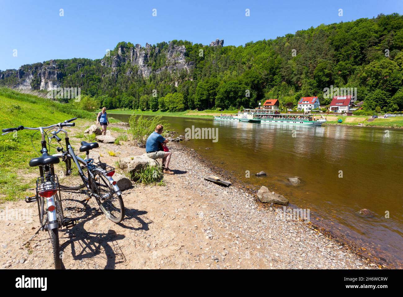 Elbe landschaftlich schöne Aussicht Deutschland Elbtal in der Sächsischen Schweiz Menschen an Land beobachten vorbeifahrende Boote und Sandsteinfelsen Stockfoto