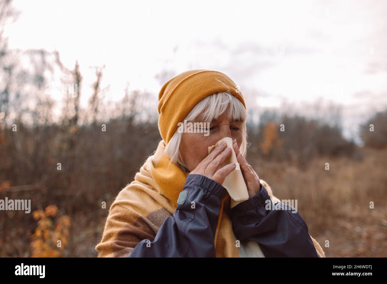 Kranke frau im erwachsenen europäischen Alter hustet und bläst ihre Nase im Park während der Herbstsaison an einem kalten Herbsttag. Stockfoto