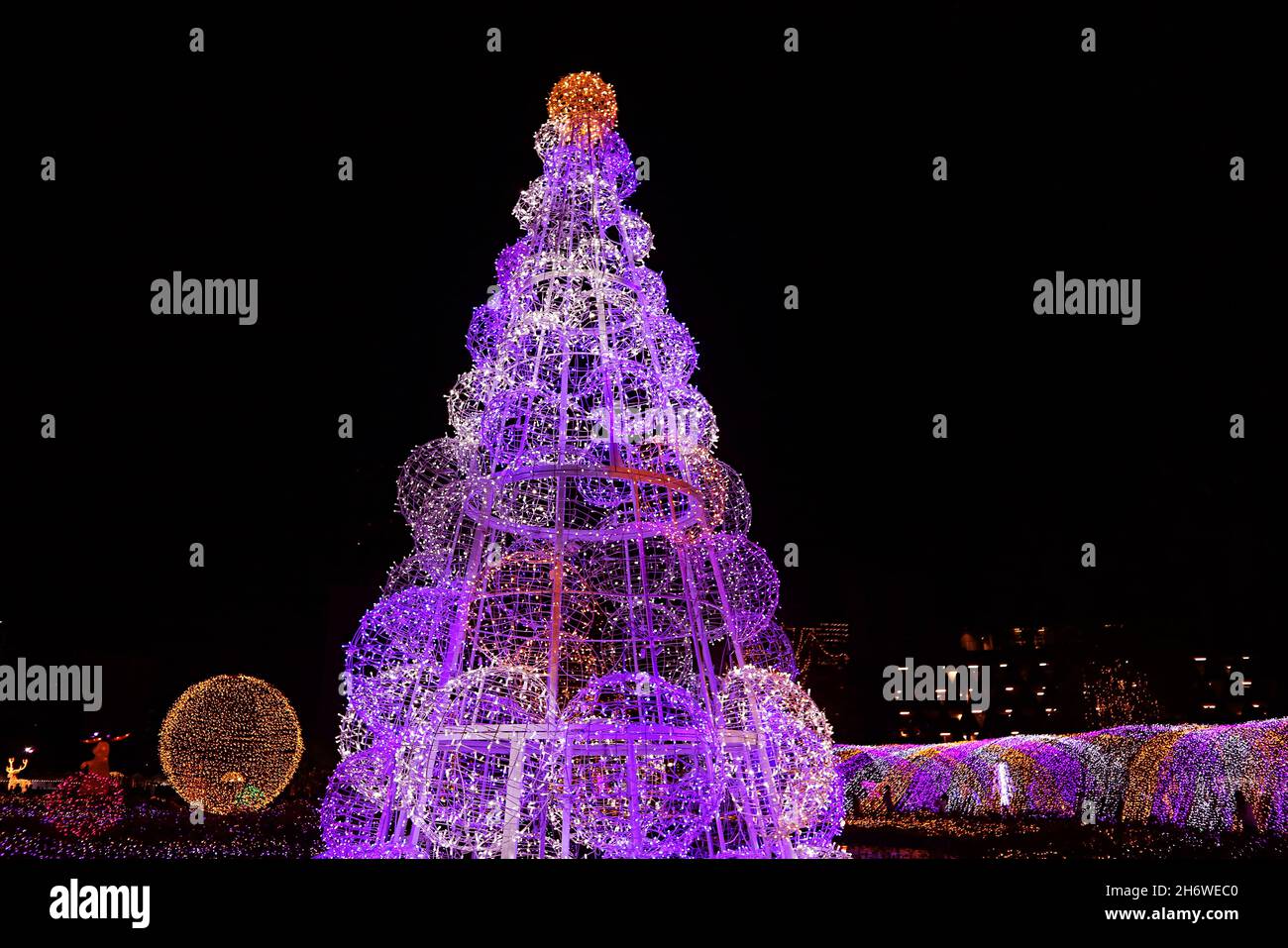 Umwerfender lila und goldener riesiger Weihnachtsbaum, der gegen den Nachthimmel glitzert Stockfoto