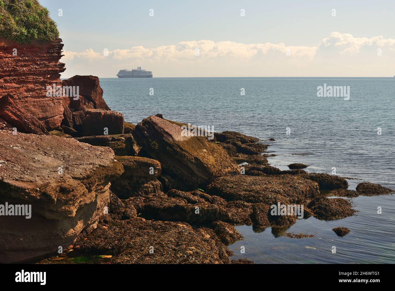 Felsen am Ende von Roundham Head, Goodrington, South Devon, mit einem Schiff, das während der Coronavirus-Pandemie vor der Küste vor Anker liegt. Stockfoto