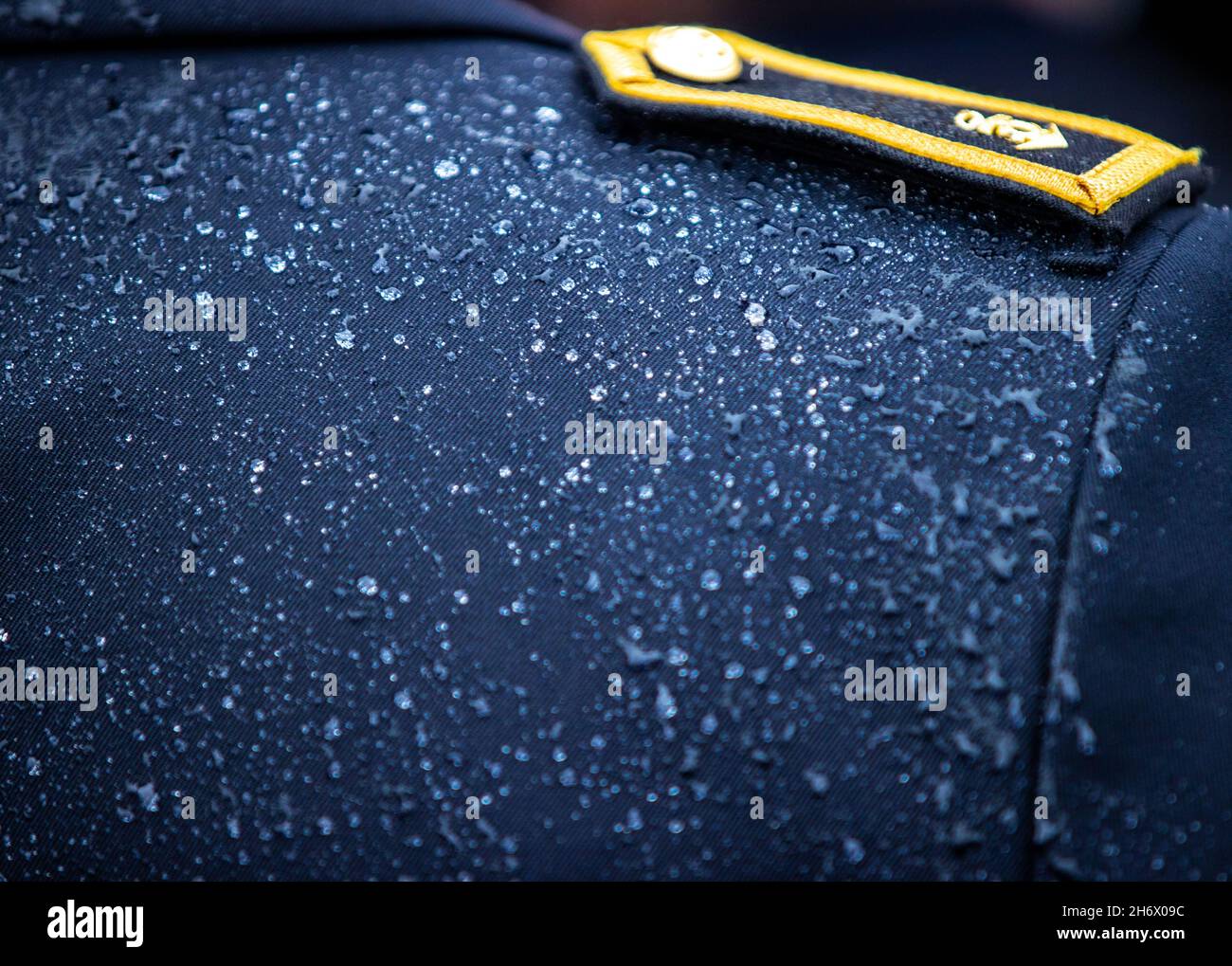 Rostock, Deutschland. November 2021. Regentropfen liegen auf der Uniformjacke eines Marinemanns auf der Korvette 'Magdeburg' auf dem Marinestützpunkt hohe Düne. Die Matrosen folgen der Befehlsübernahme durch Corvette Captain Bianca Seifert. Ab dem nächsten Jahr soll die Korvette 'Braunschweig' an mehreren multinationalen Manövern unter dem Kommando von Seifert teilnehmen. Sie ist die erste weibliche Kommandantin einer Korvettenbesatzung in der deutschen Marine. Quelle: Jens Büttner/dpa-Zentralbild/dpa/Alamy Live News Stockfoto