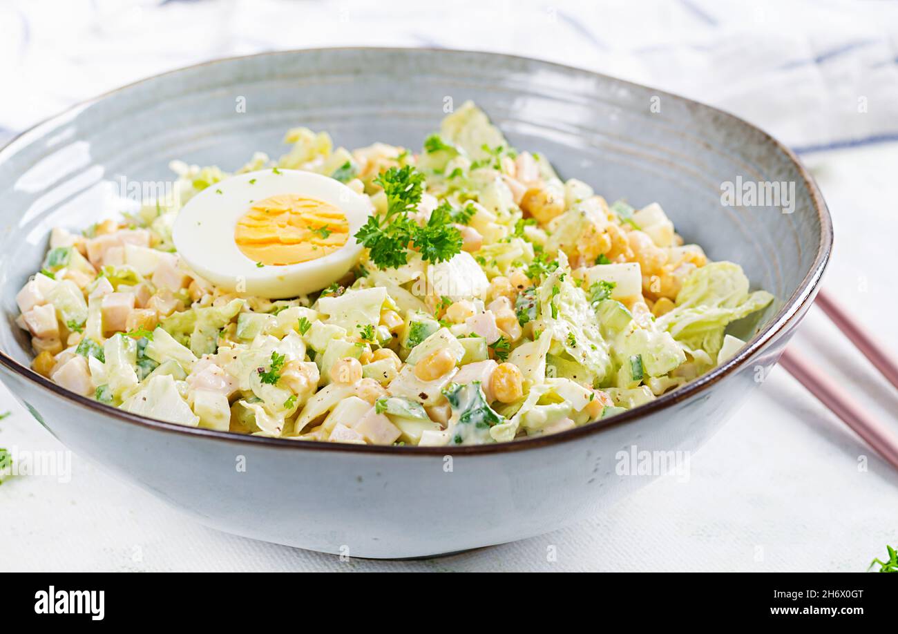 Festlicher Salat mit Schinken, Gurken, gekochten Eiern, Mais und Mayonnaise auf rustikalem Geschmack. Stockfoto