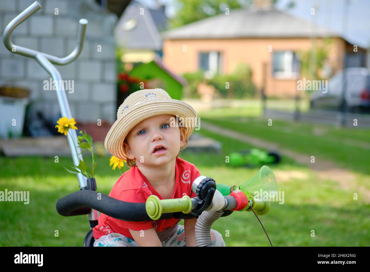 Porträt eines niedlichen kleinen Mädchens in einem Sonnenhut, das auf einem Fahrrad sitzt und an einem sonnigen Tag in Polen auf die Kamera schaut Stockfoto