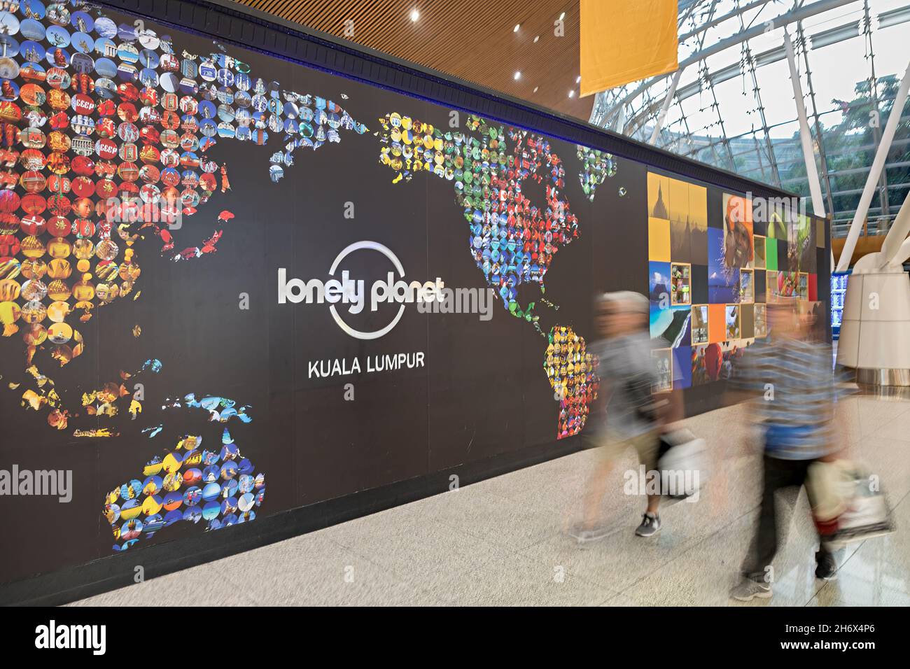 Lonely Planet Wall im Flughafen mit zu Fuß verschwommenen Menschen, Kuala Lumpur, Malaysia Stockfoto
