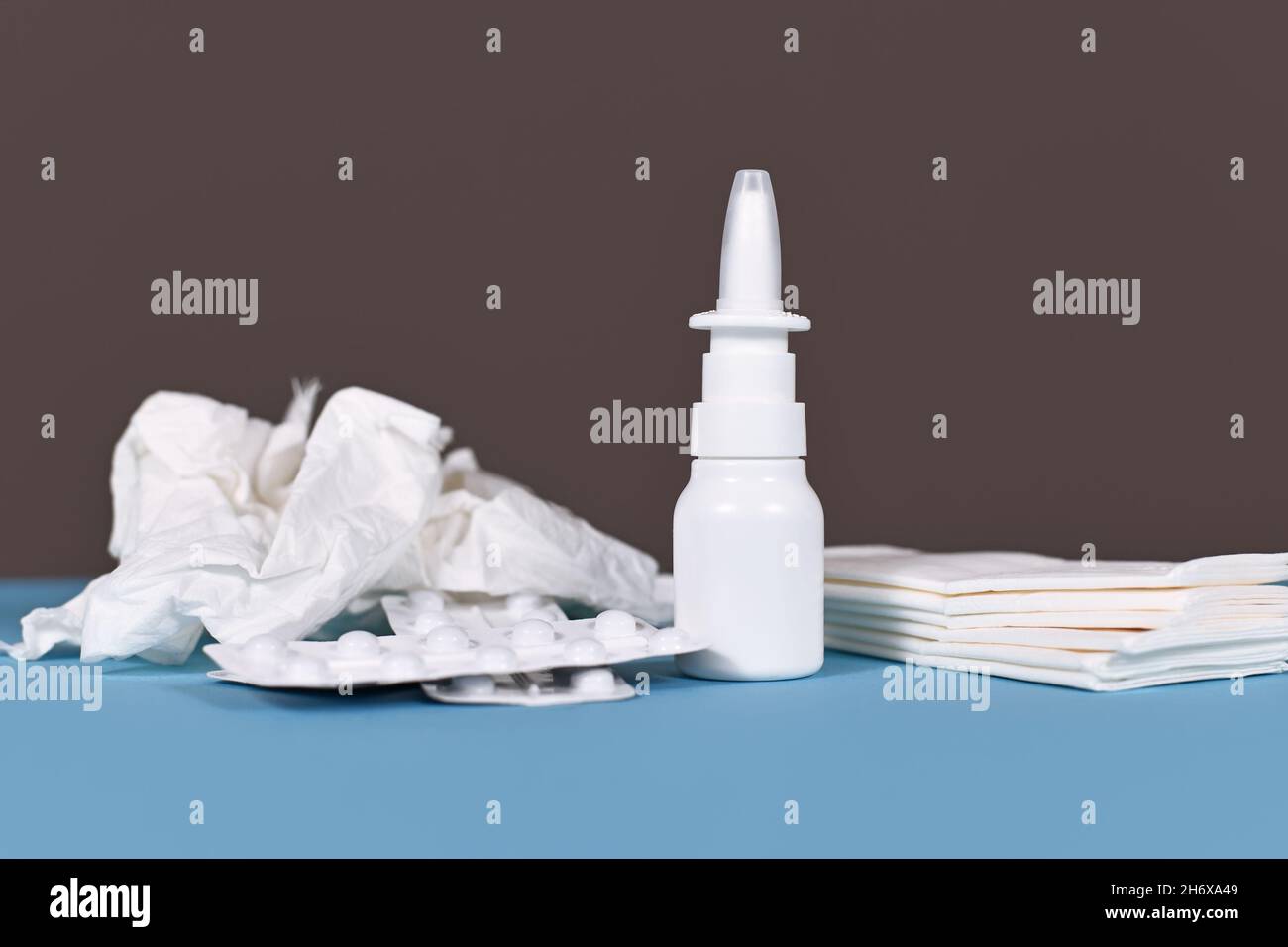 Weiße Flasche mit Nasenspray mit zerbröckeltem Gewebe und Tabletten gegen Erkältung auf blauem Tisch Stockfoto