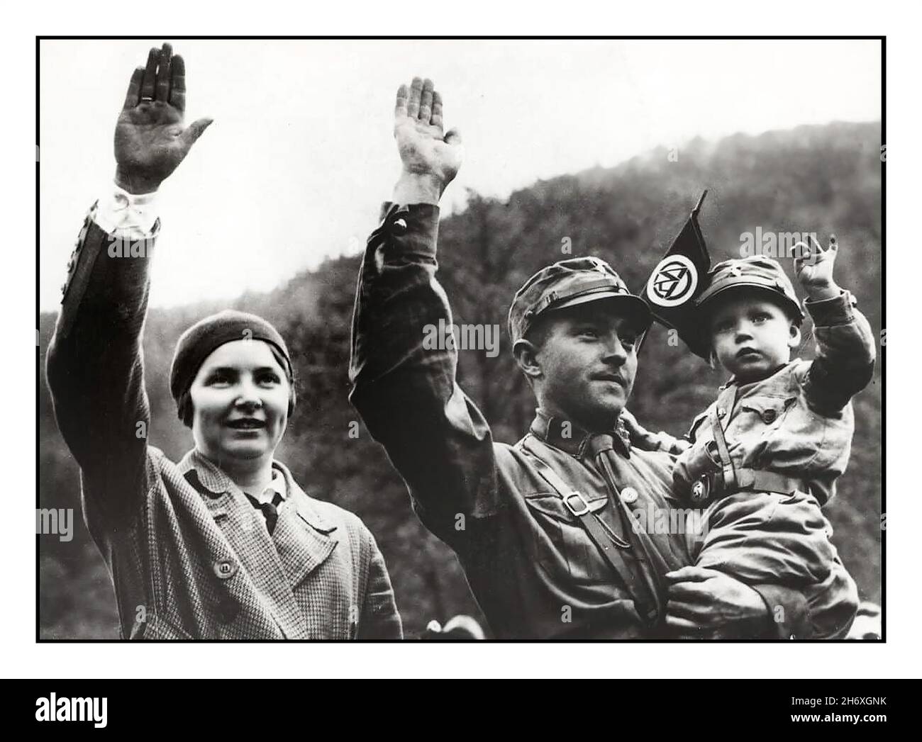 SA Sturmabteilung 1930s Archiv Nazi-deutsche dreiköpfige Familie, die den Heil-Hitler-Gruß überlässt, wobei der Vater die Uniform der SA-Sturmabteilung in braunen Hemden des paramilitärischen nazi-Flügels trägt. Sein Sohn trägt eine ähnliche Kinderuniform und winkt mit der Flagge der SA-Sturmabteilung Nazi-Deutschland. Die als ideal arierisch-deutsche Familie der 1930s Stockfoto