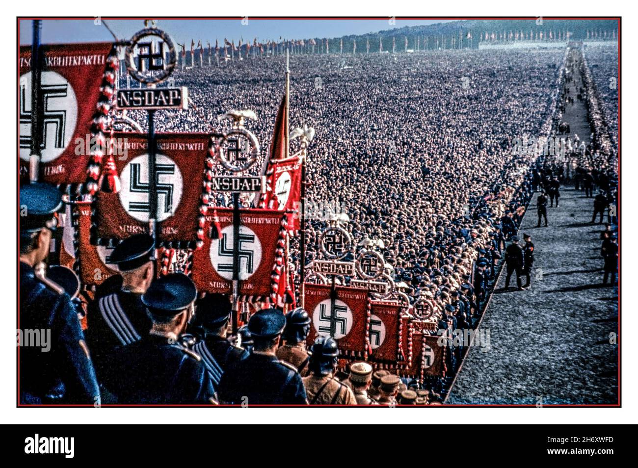 1930s NSDAP-Banner und Hakenkreuz-Emblem im Vordergrund, in Farbe, mit Transparenten und Fahnen im überfüllten Hauptaula im Freien, mit Tausenden von Nazi-Parteiunterstützern und seltenen Farbbildern, mit NSDAP-Bannern und Hakenkreuz-Emblem im Vordergrund. Die Nazi-Partei offiziell die nationalsozialistische Deutsche Arbeiterpartei (NSDAP) war eine rechtsextreme politische Partei in Deutschland, die zwischen 1920 und 1945 aktiv war und die Ideologie und Propaganda des Nationalsozialismus und der Nazi-Partei unter der Führung des ‘Führers’ Adolf Hitler Nazi-Deutschland schuf und unterstützte Stockfoto