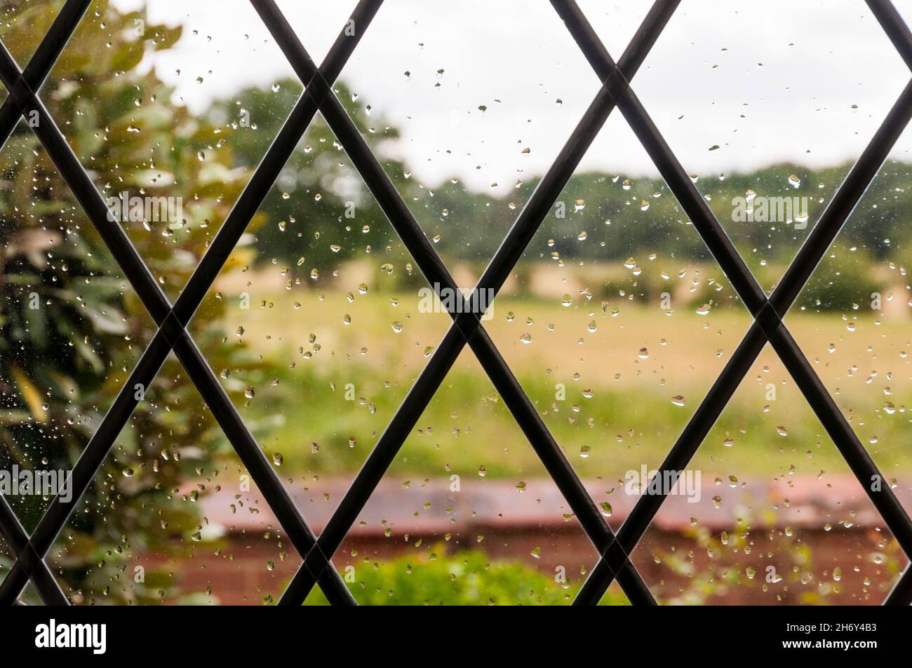 Unfokussierte Landschaft durch Regentropfen auf rautenverglasten Fenstern der Hütte. Stockfoto