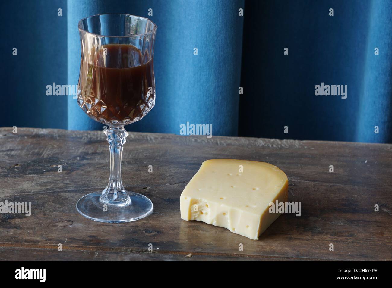 Cheddar-Käsestück auf einem Holztisch neben einem Weinglas Stockfoto