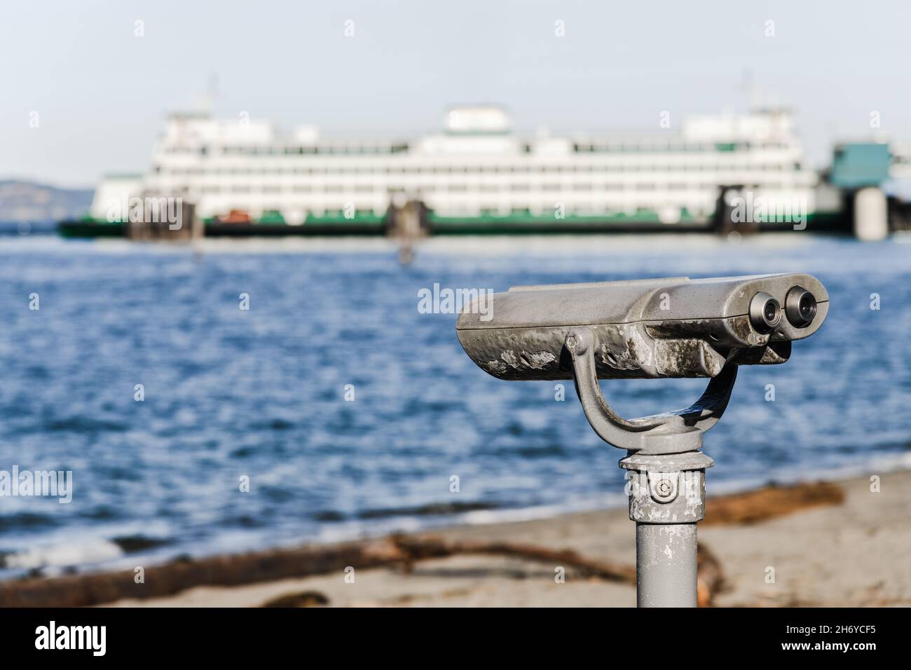 Ein Paar Ferngläser aus Metall auf einem festen Stand blicken auf ein Meer und ein Fährschiff, das nicht im Fokus steht Stockfoto