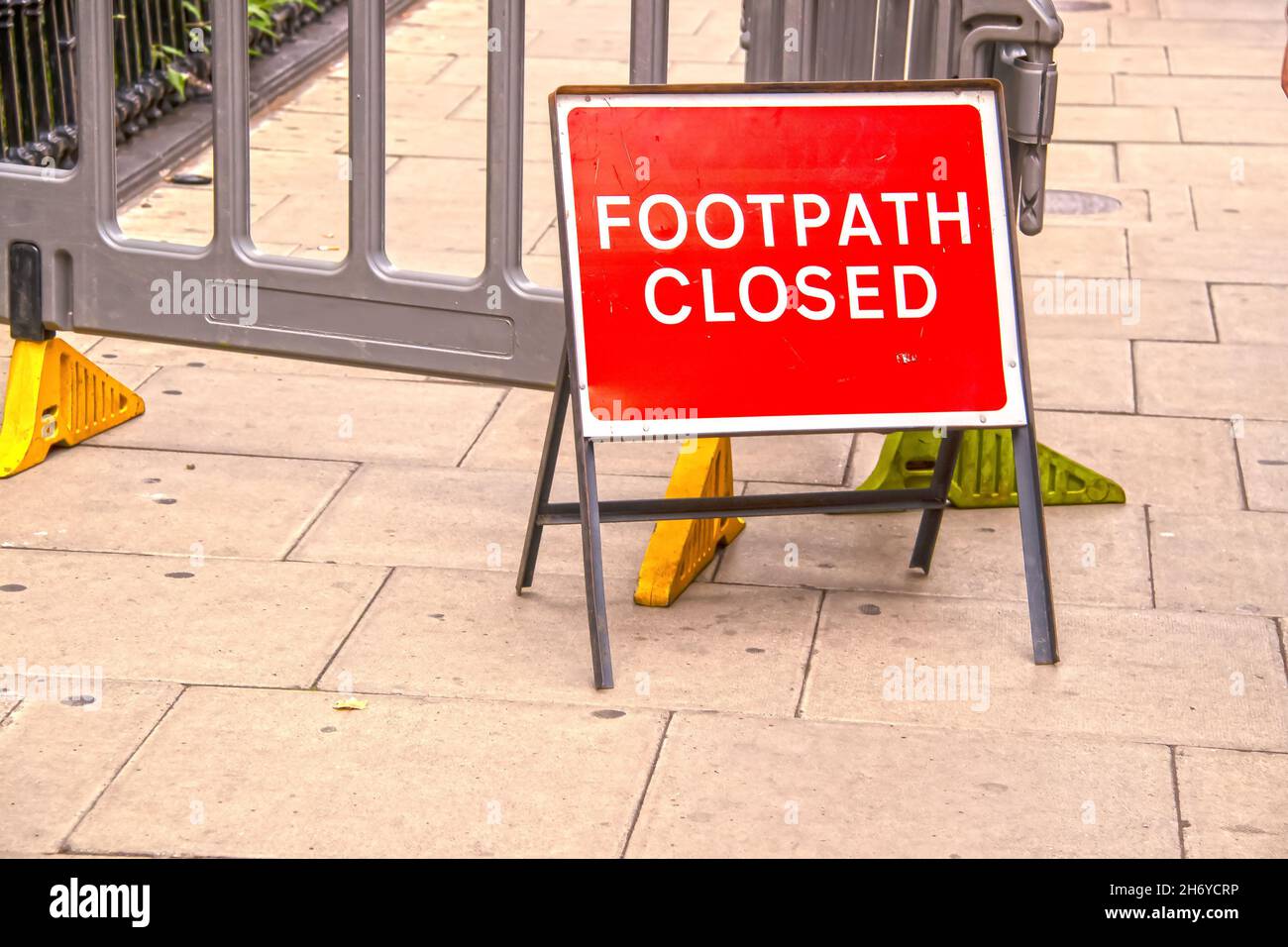 Temporäres rotes Fußwegenschild vor dem Plastikzaun auf dem Londoner Bürgersteig - selektiver Fokus Stockfoto