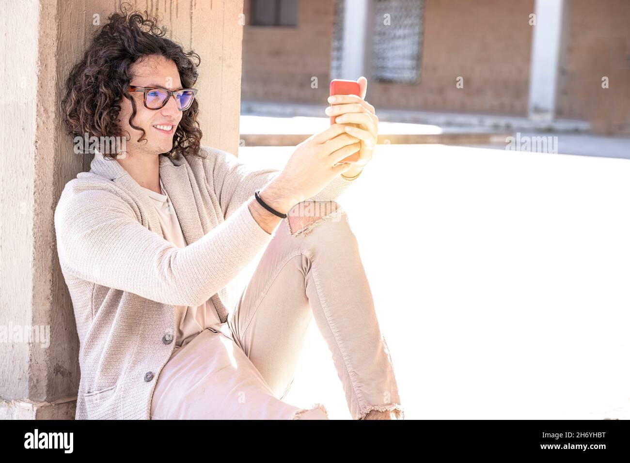 Seitenansicht eines jungen Mannes, der auf einer Treppe im Freien sitzt und das Telefon in den Händen hält Stockfoto