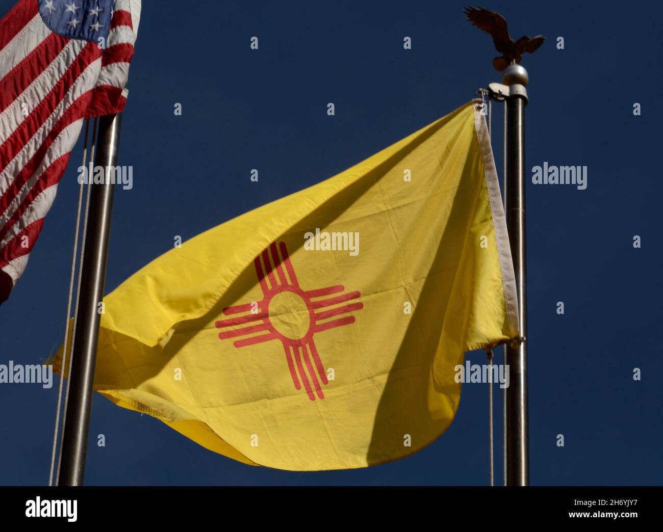 Die Staatsflagge von New Mexico mit ihrem indianischen Sonnensymbol fliegt neben einer Flagge der Vereinigten Staaten in Santa Fe, New Mexico. Stockfoto