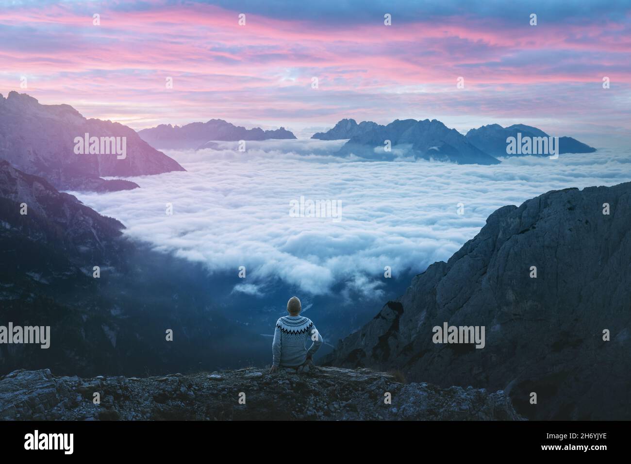 Ein Tourist, der über dem Nebel am Rand einer Klippe in den Dolomiten sitzt. Lage Auronzo rifugio im Nationalpark Tre Cime di Lavaredo, Dolomiten, Trentino-Südtirol, Italien Stockfoto