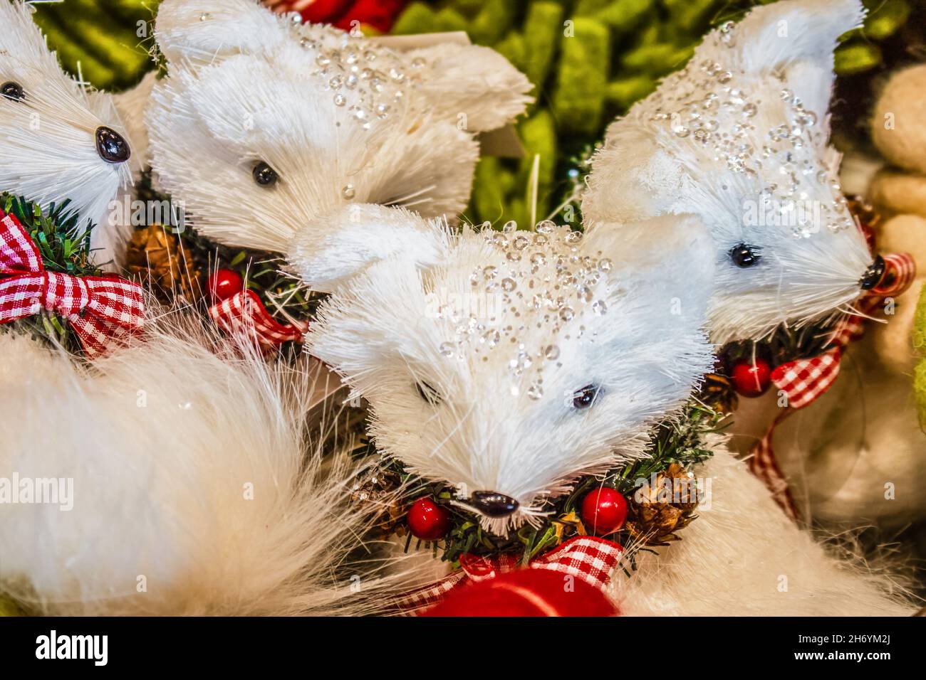 Weisse Fuchs-Weihnachtsschmuck mit Juwelen auf ihren Köpfen mit roten Gingham-Schleifen und Beeren - selektiver Fokus Stockfoto
