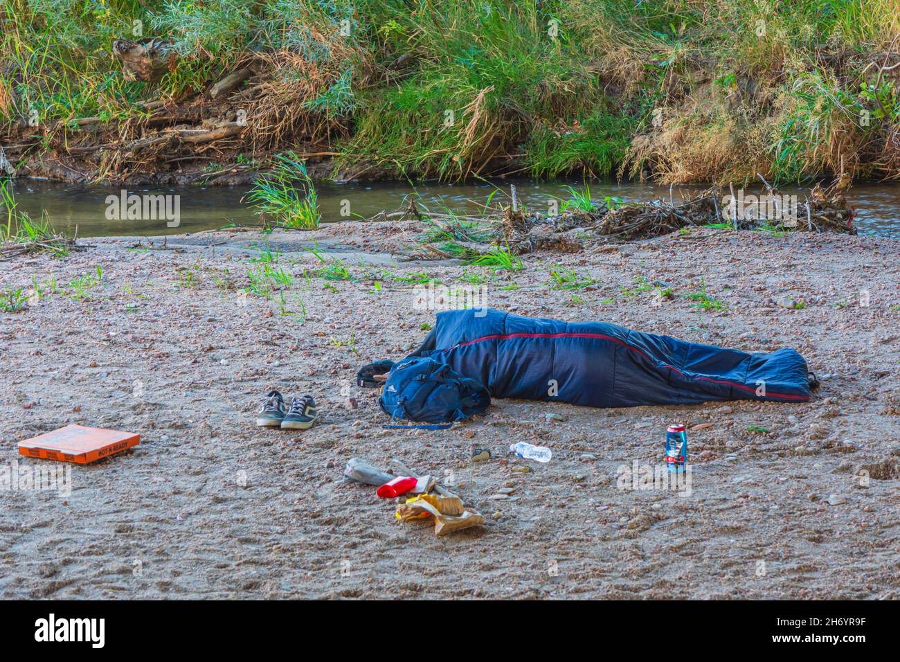 Junge Obdachlose schlafen im Schlafsack unter der Autobahnüberführung auf der Sandbank von East Plum Creek, Castle Rock Colorado USA. Foto aufgenommen im Oktober. Stockfoto