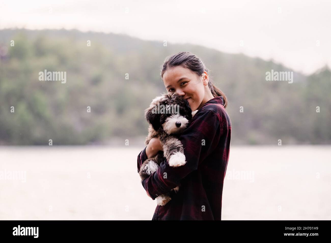 An einem warmen Sommertag umarmt sich der Schäferhund und mit der Frau auf einem Dock am See Stockfoto