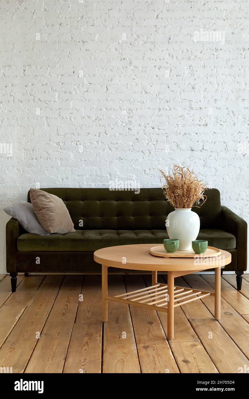 Komfortable weiche Couch mit Kissen in der Nähe von runden Tisch platziert dekorieren mit Vase mit getrockneten Pflanzen in Lounge im Loft-Stil mit Backsteinwand und gestaltet Stockfoto