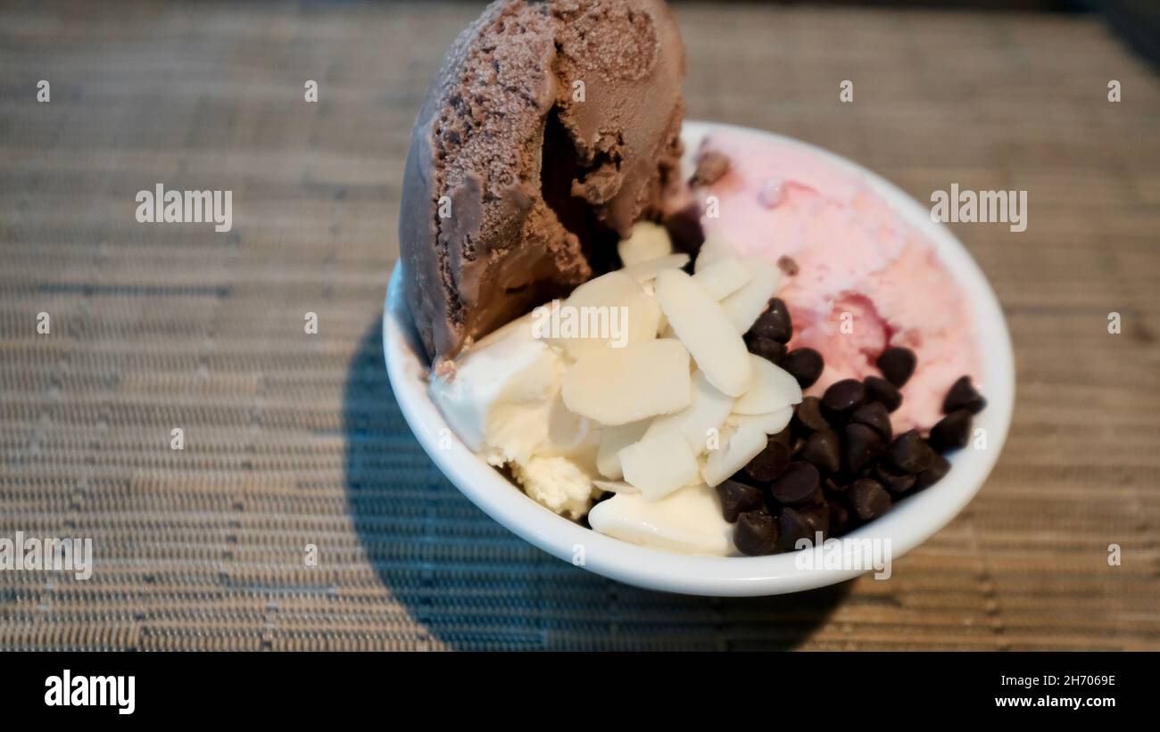Eis aus Schokolade, Vanille und Erdbeere mit Schokoladensplitter und in Scheiben geschnittenen Mandeln in einer Schüssel Stockfoto