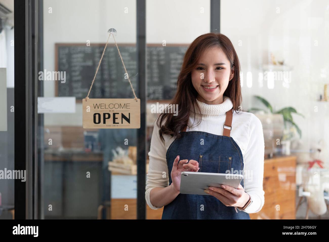 Porträt einer lächelnden asiatischen Unternehmerin, die hinter ihrem Café-Tresen mit offenem Schild steht Stockfoto