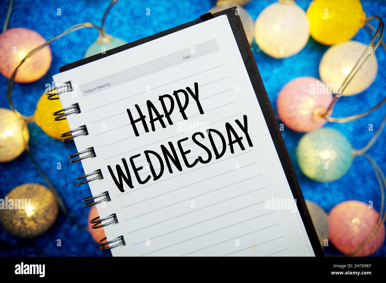 Happy Wednesday Text Notizblock Mockup und LED-Baumwollkugeln Dekoration auf blauem Bokeh Hintergrund Stockfoto