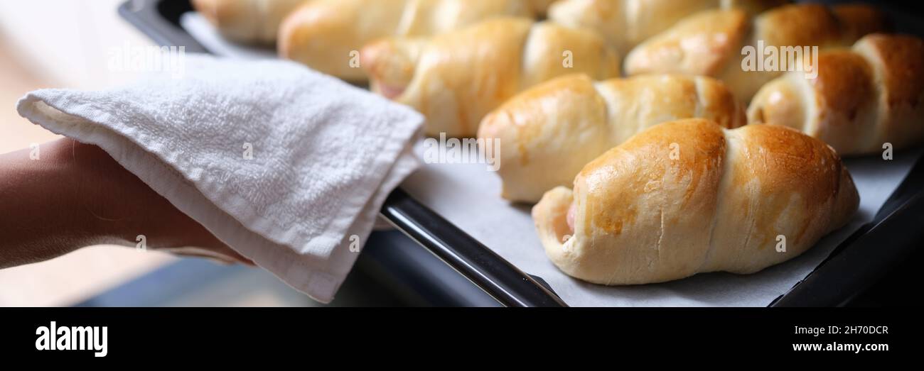Hausfrau nimmt heiße leckere Brötchen aus dem Ofen auf Backblech Nahaufnahme Stockfoto