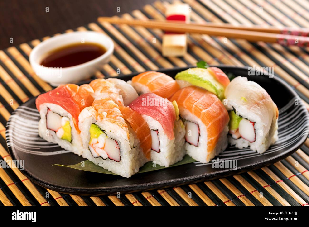 Set aus Regenbogen-Uramaki-Sushi-Rollen mit Thunfisch, Lachs und Avocado, serviert im Restaurant auf Bambusmatte Stockfoto