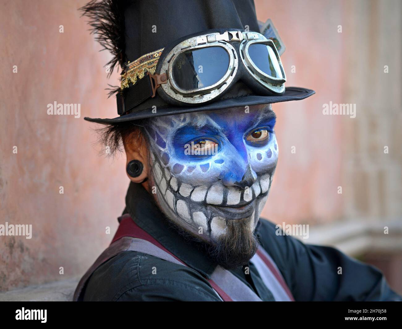 Kostümierter junger mexikanischer Yucatecan-Mann mit gruseliger blauer Gesichtsbemalung und schwarzem Zylinderhut blickt auf den Zuschauer am Tag der Toten (Día de los Muertos). Stockfoto